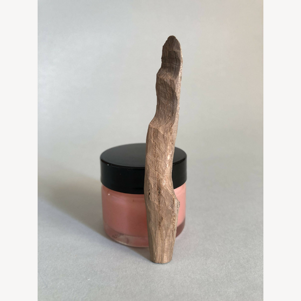 Cuillère à cosmétiques en bois, manche vertical, posée sur un pot à couvercle noir.