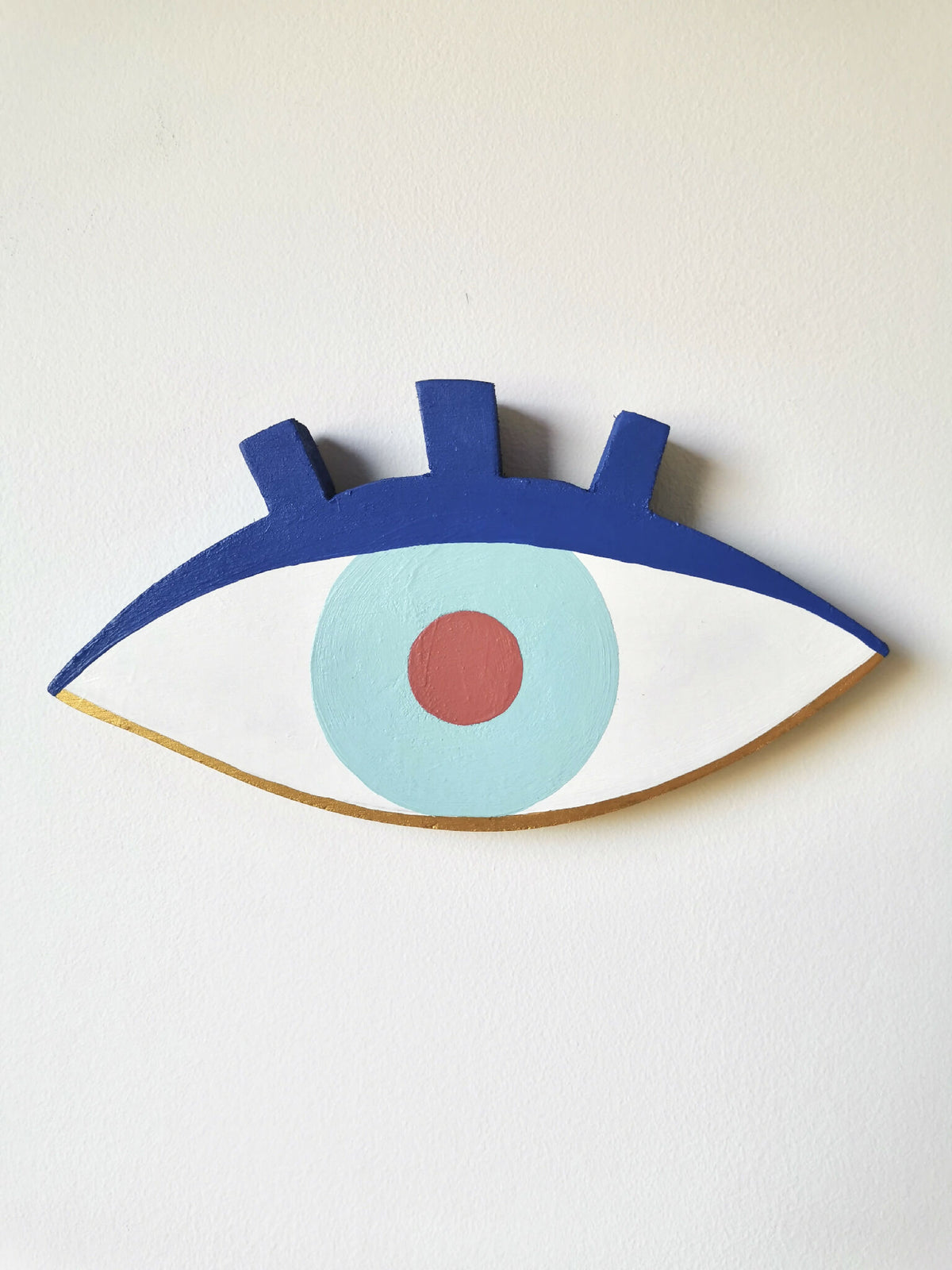 Œil en peinture sur bois, fond blanc, iris bleu clair et pupille orange.
