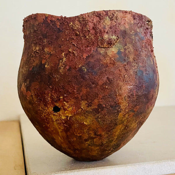 Vase en métal oxydé, teintes brun rouge et mauve, forme arrondie, fond visible.