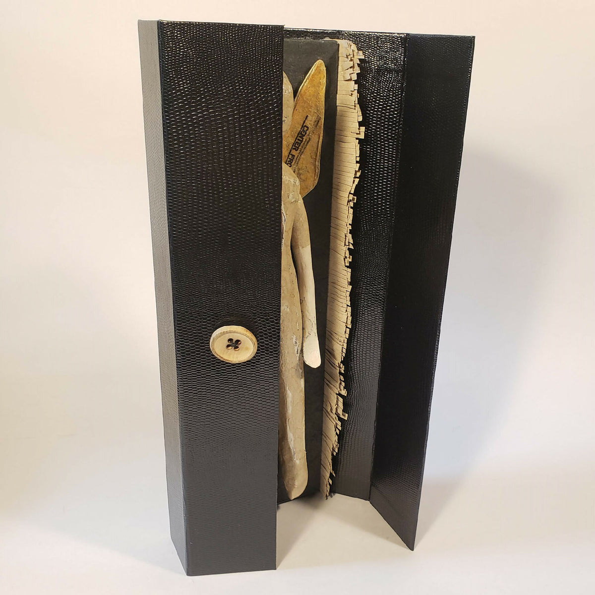 Sculpture papier de poupée aux ailes dorées, vue latérale dans un écrin noir ouvert