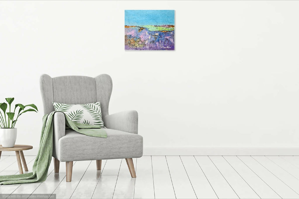 Petit tableau abstrait sur mur blanc, au-dessus d’un fauteuil gris, peinture colorée
