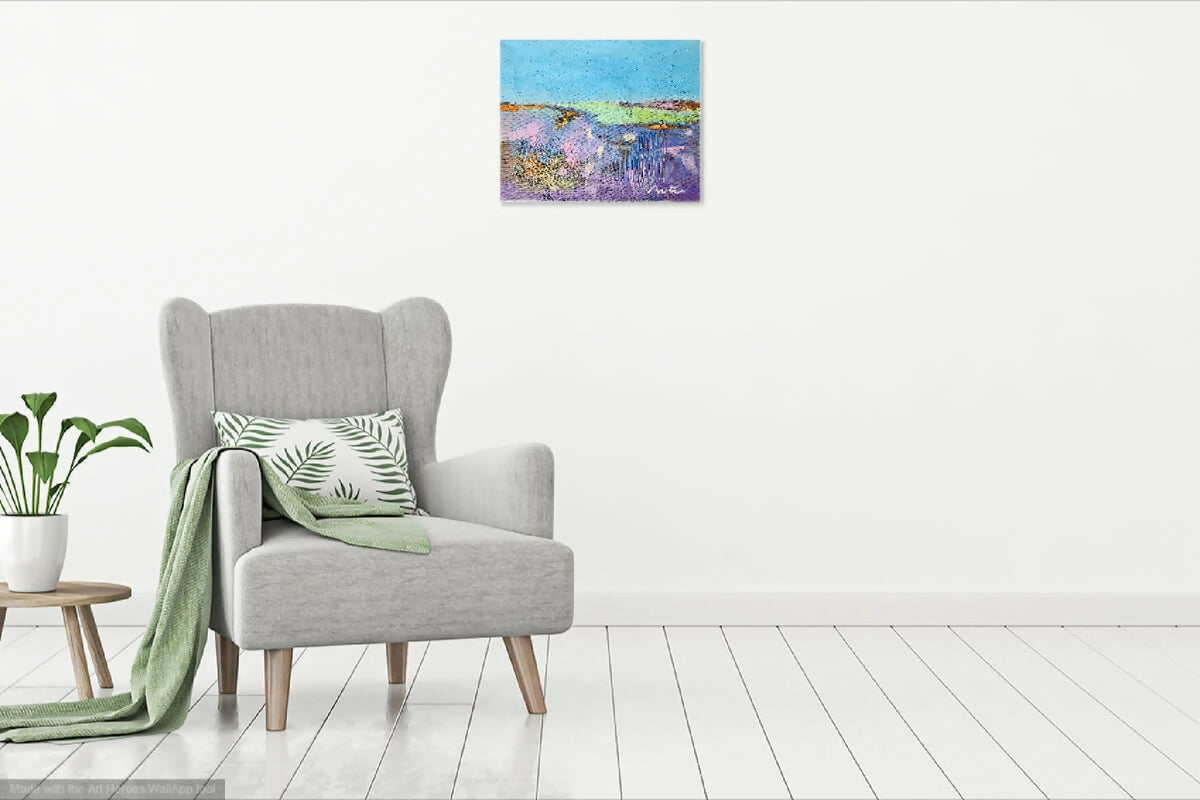 Petit tableau abstrait sur mur blanc, au-dessus d’un fauteuil gris, peinture colorée