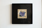 Tableau encadré noir avec collage abstrait bleu et violet sur papier clair.
