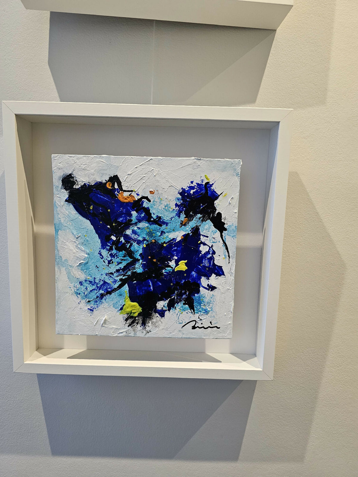 Peinture abstraite bleu et noir à éclats jaunes, dans un cadre blanc en niche