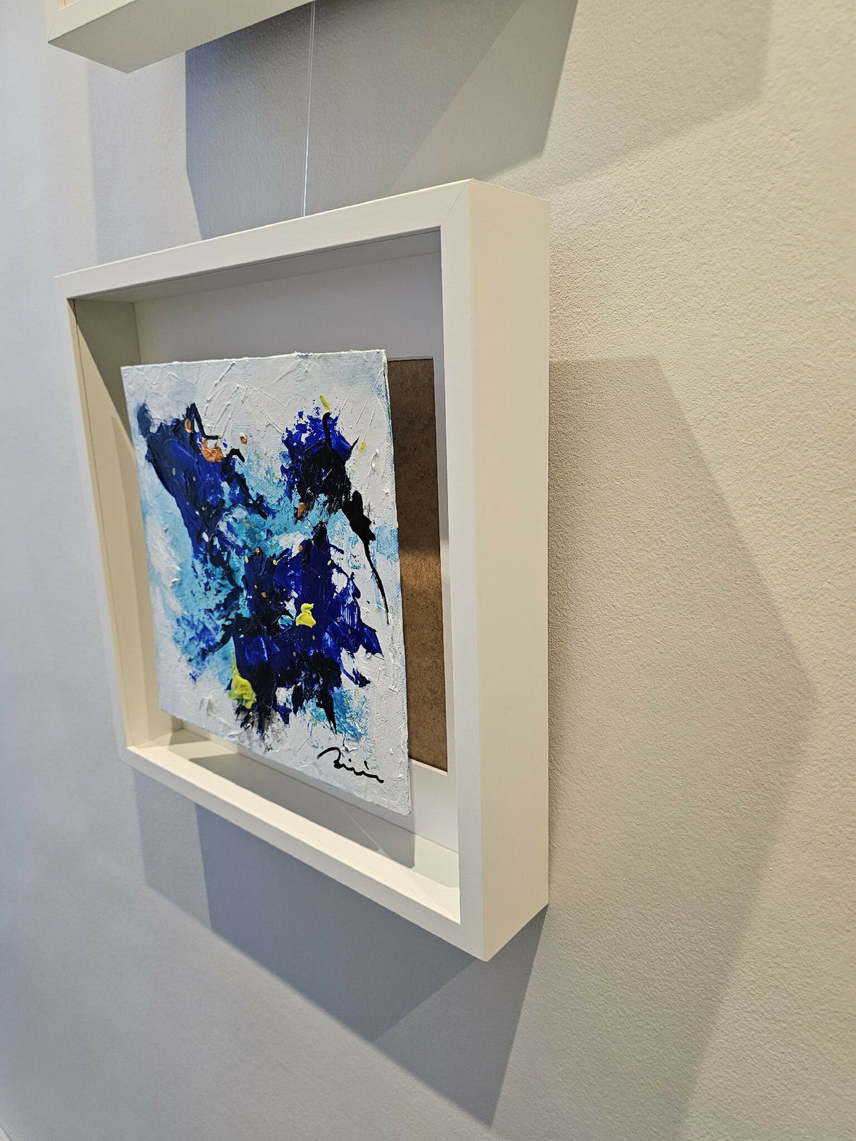Peinture abstraite bleu et noir avec éclats jaunes, cadre blanc vu de côté