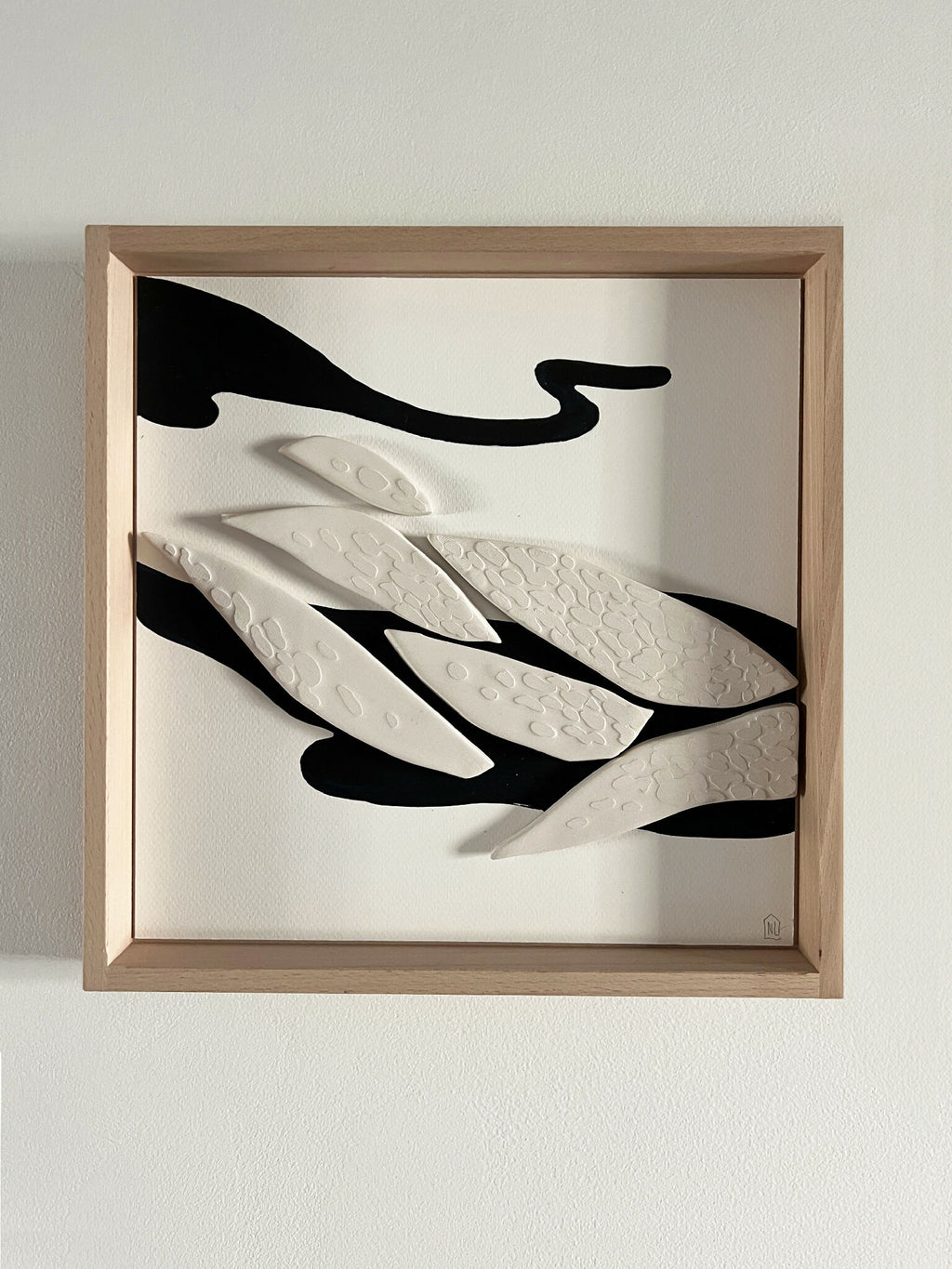 Tableau abstrait encadré, formes ondulées noir et blanc sur fond clair.