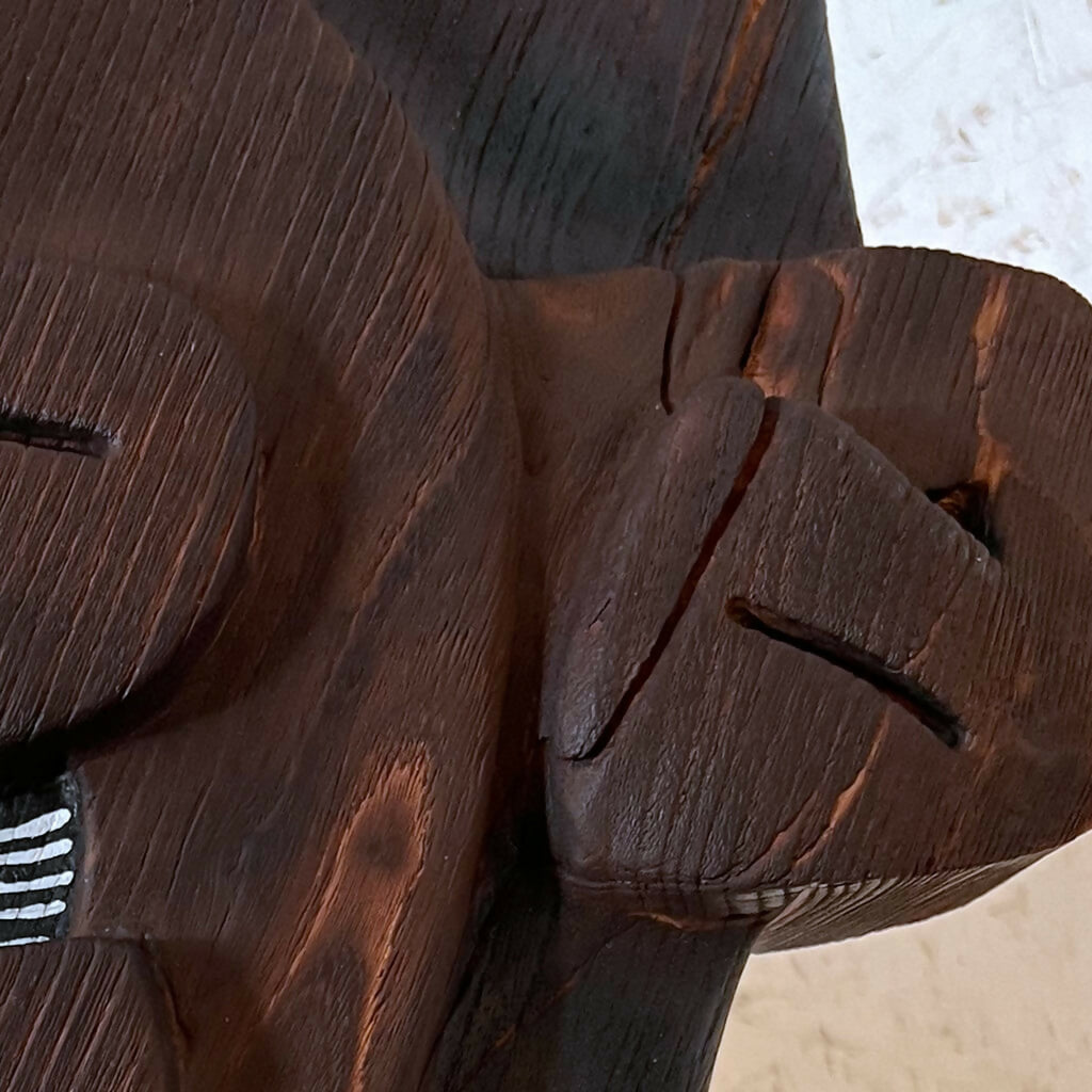 Détail de la sculpture en bois foncé avec relief et lignes gravées