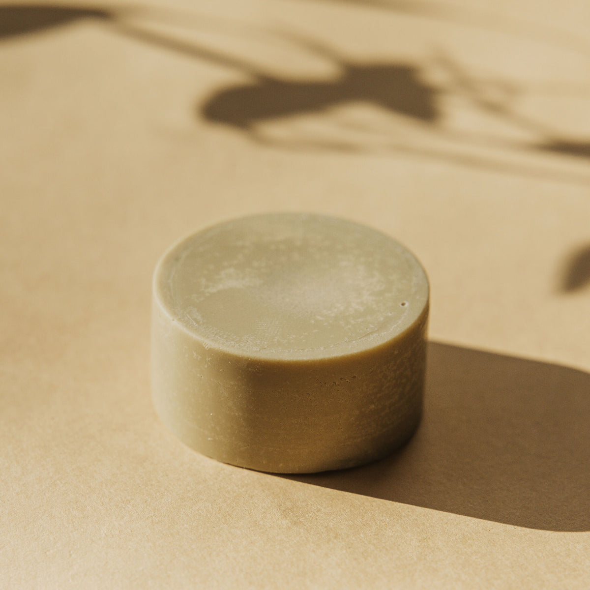 Déodorant solide Faveur rond, posé sur une surface beige
