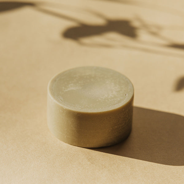 Déodorant solide Faveur rond, posé sur une surface beige