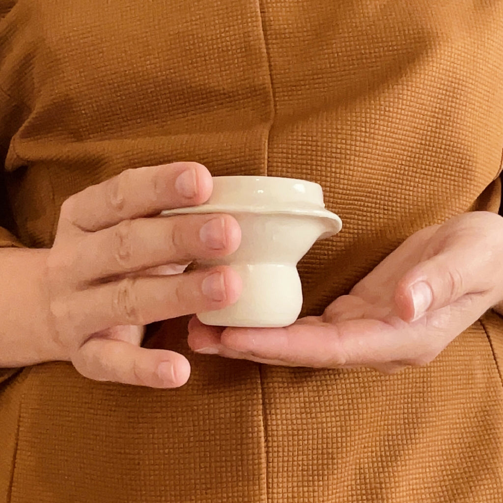 Tasse à café en céramique beige tenue par deux mains, anse visible