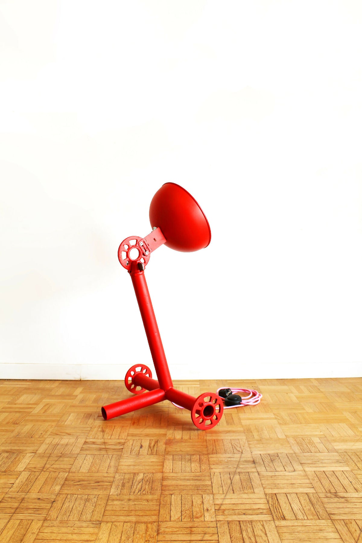 Lampe rouge sur trépied avec abat-jour conique, câbles spiralés visibles au sol