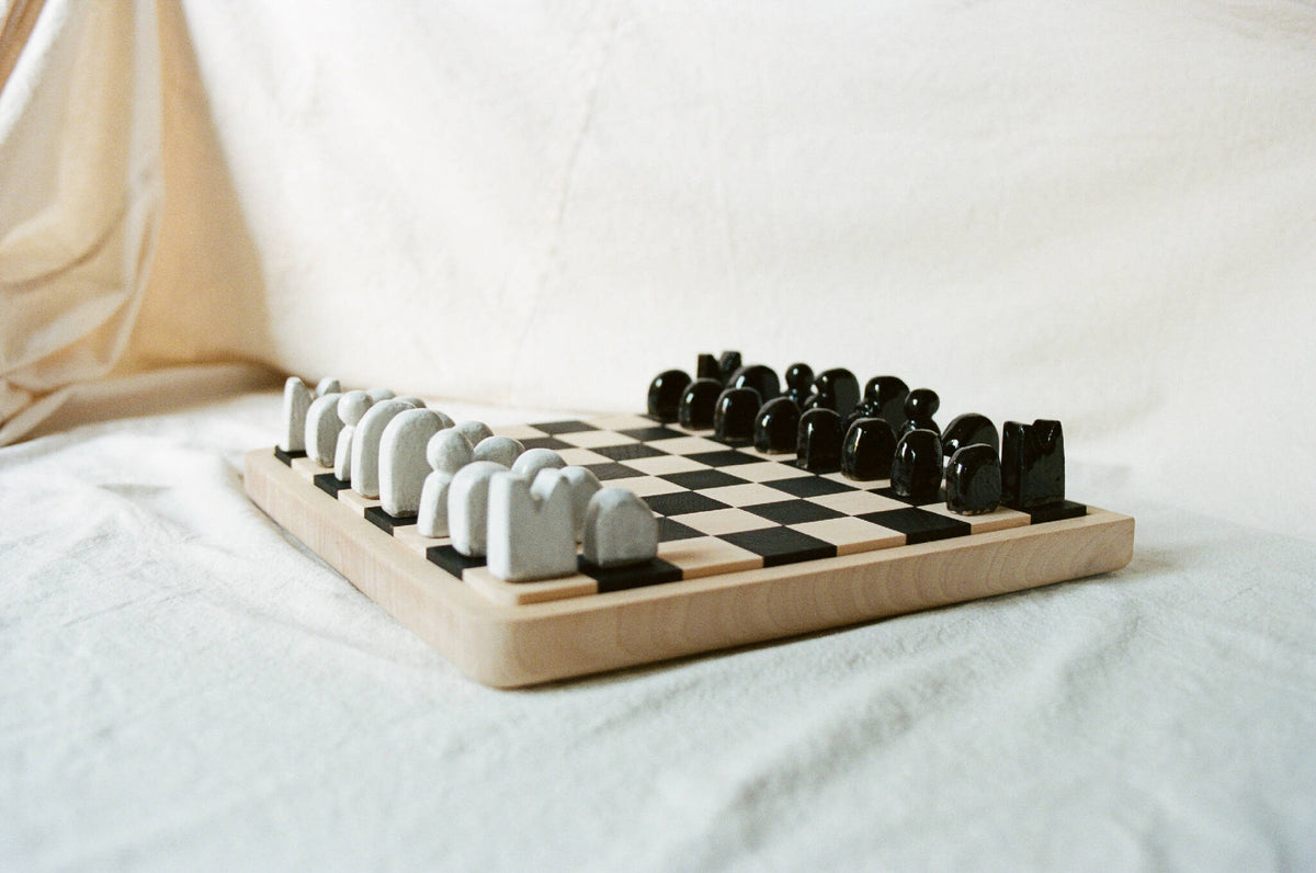 Échiquier en bois avec damier noir et blanc, rangées de pièces en céramique blanches et noires