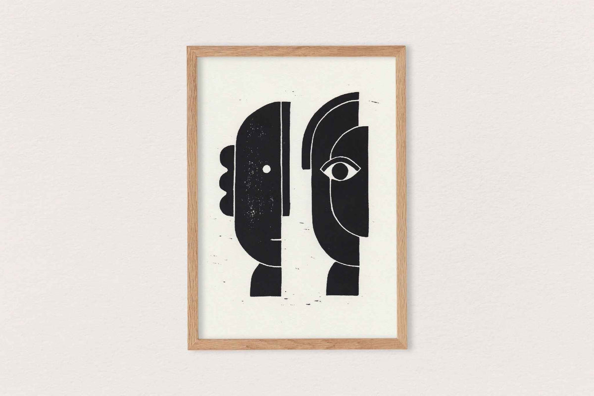 Linogravure encadrée : visages abstraits noirs, lignes blanches, fond clair.