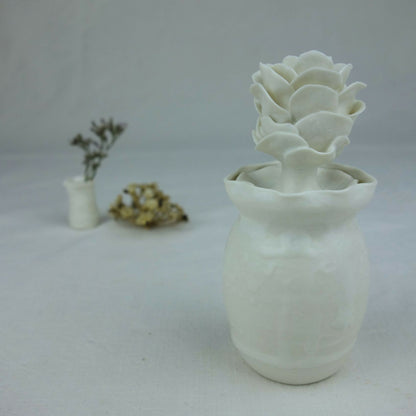 Vase en céramique blanc avec fleurs en relief empilées au centre, vue de profil.