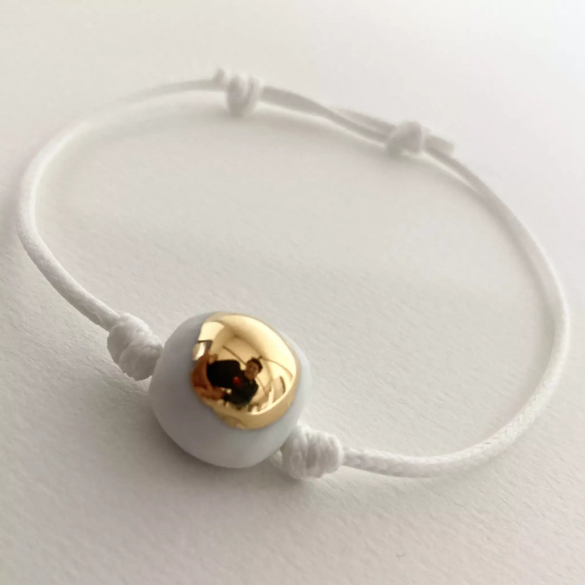 Bracelet cordon blanc et perle dorée ronde, nœuds en porcelaine