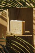 Savon en barre crème avec logo gravé, posé sur une planche de bois.