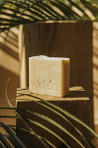 Savon en barre crème avec logo gravé, posé sur une planche de bois.