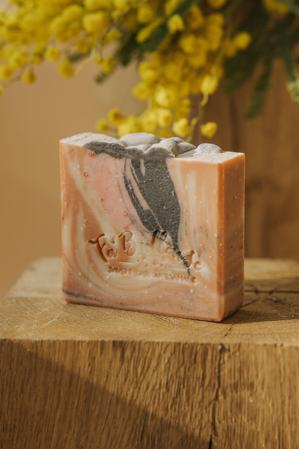 Savon en barre marbrée beige, rosé et noir, posé sur une planche en bois.
