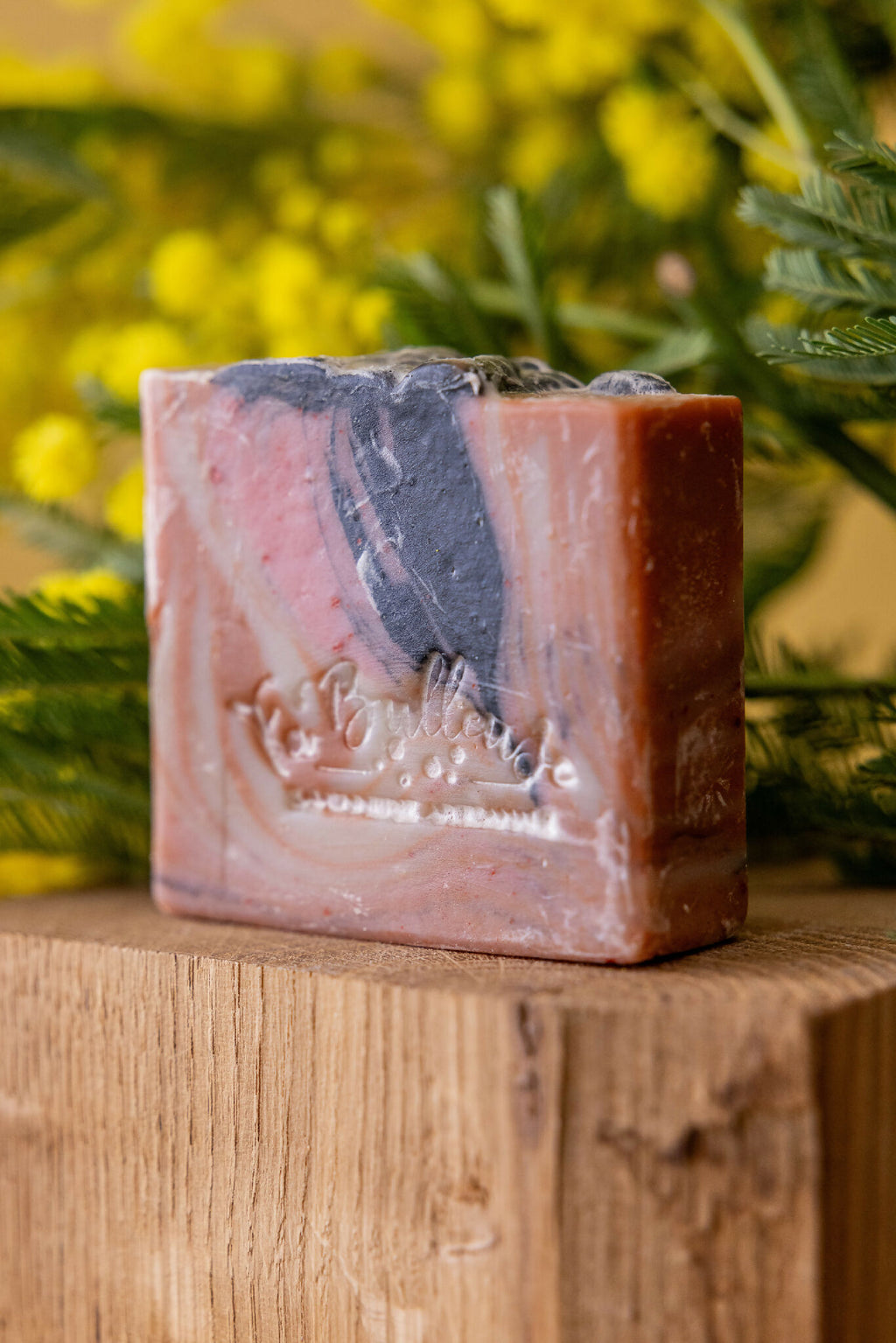 Savon artisanal en barre marbrée rosé, beige et noir sur plateau en bois.