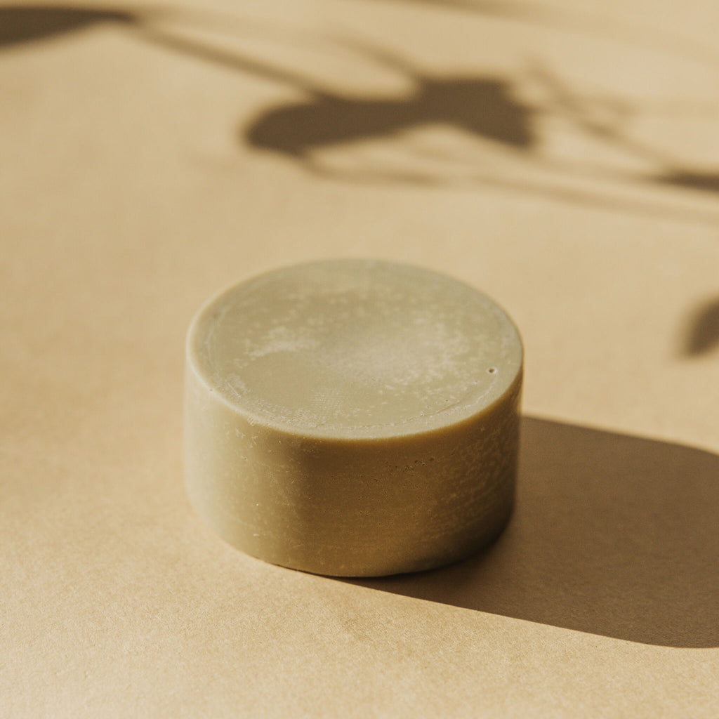 Déodorant solide Faveur rond, posé sur une surface beige