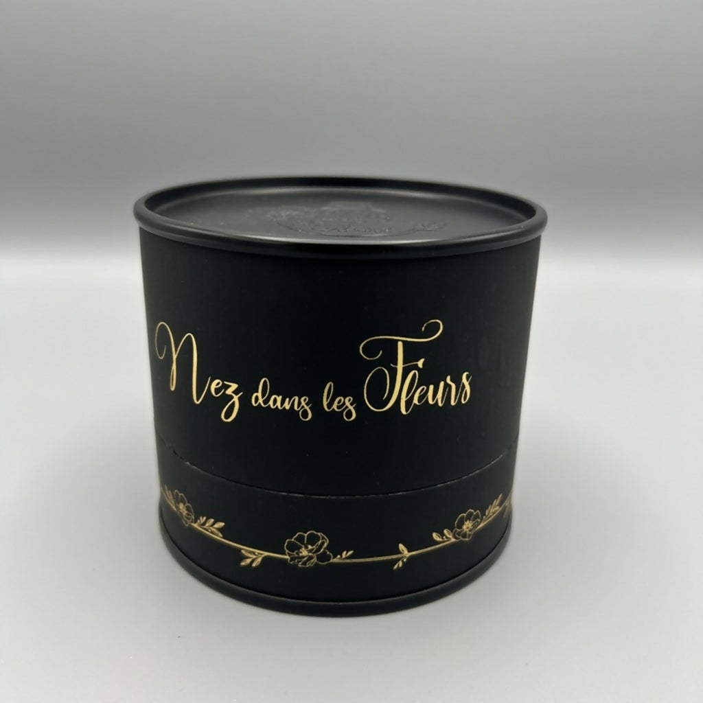 Bougie cylindrique noire « Nez dans les Fleurs » avec inscription dorée.