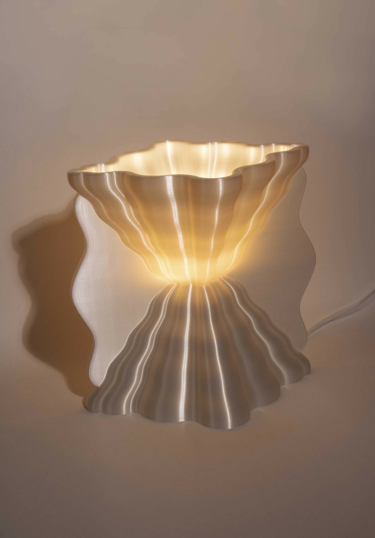 Lampe murale argentée, abat-jour ondulé, lumière chaude allumée.