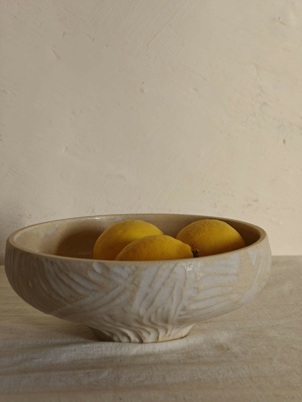 Bol crème sculpté avec motifs, rempli de citrons jaunes.