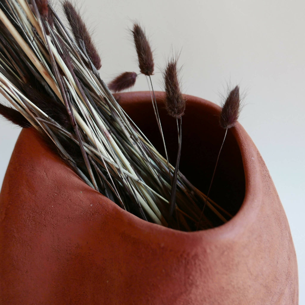 Vase en céramique rouge BRAZIL, gros plan sur l’ouverture et les herbes séchées.