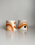 Deux grandes tasses trapèze en céramique blanche, motifs beige et orange.