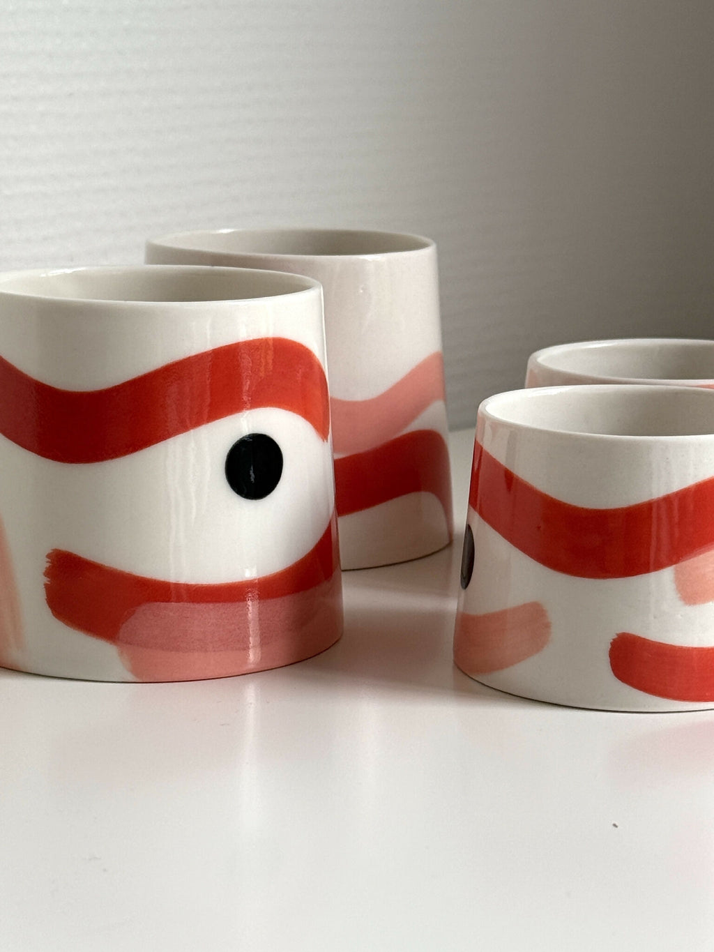 Ensemble de grandes tasses trapèze en céramique blanche, motifs rouge et beige.