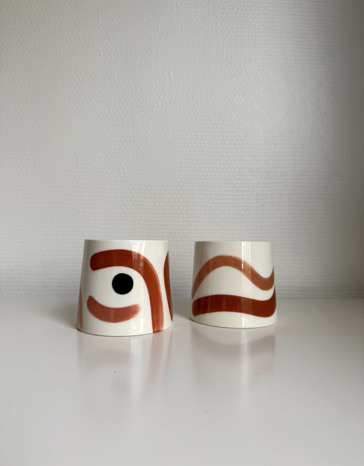 Deux grandes tasses trapèze en céramique blanche, motifs brun et rouge.