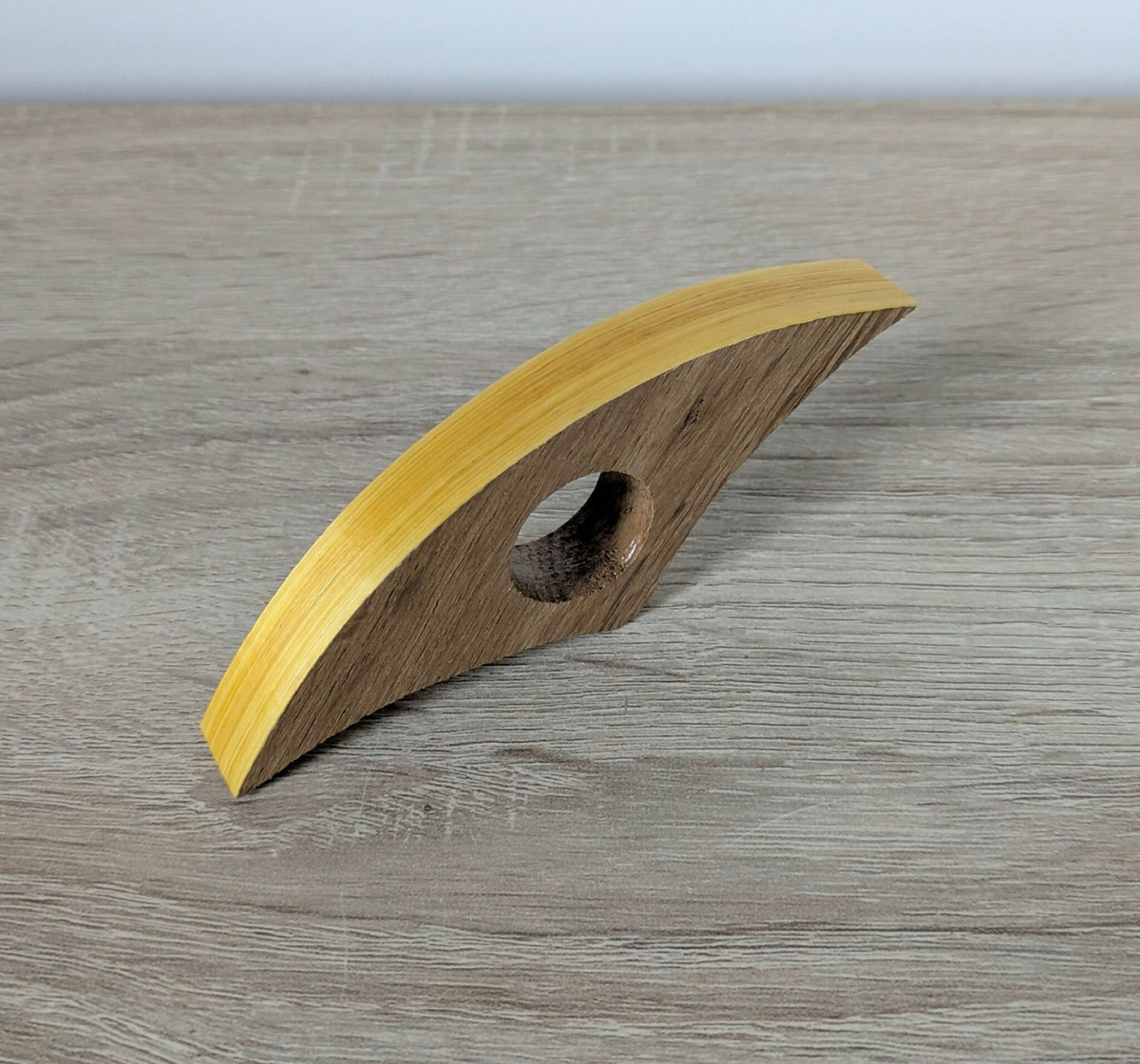Anneau de lecture incurvé en bois sombre, liseré jaune en paille, trou circulaire.