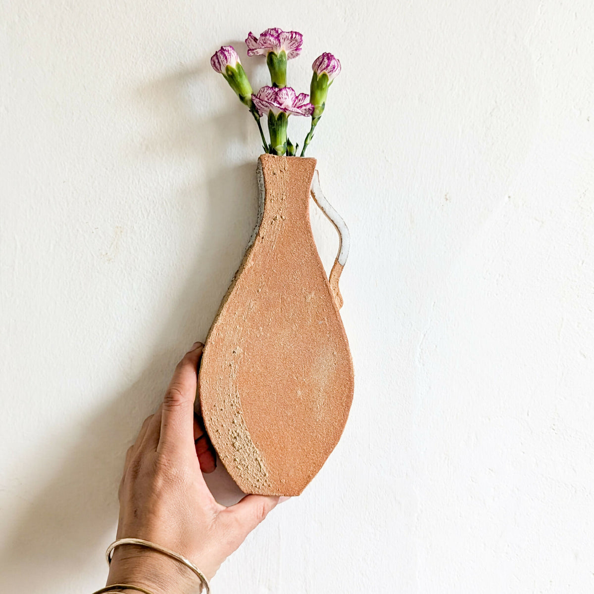 Vase mural en terre cuite, main tenant le vase, bouquet de fleurs violettes