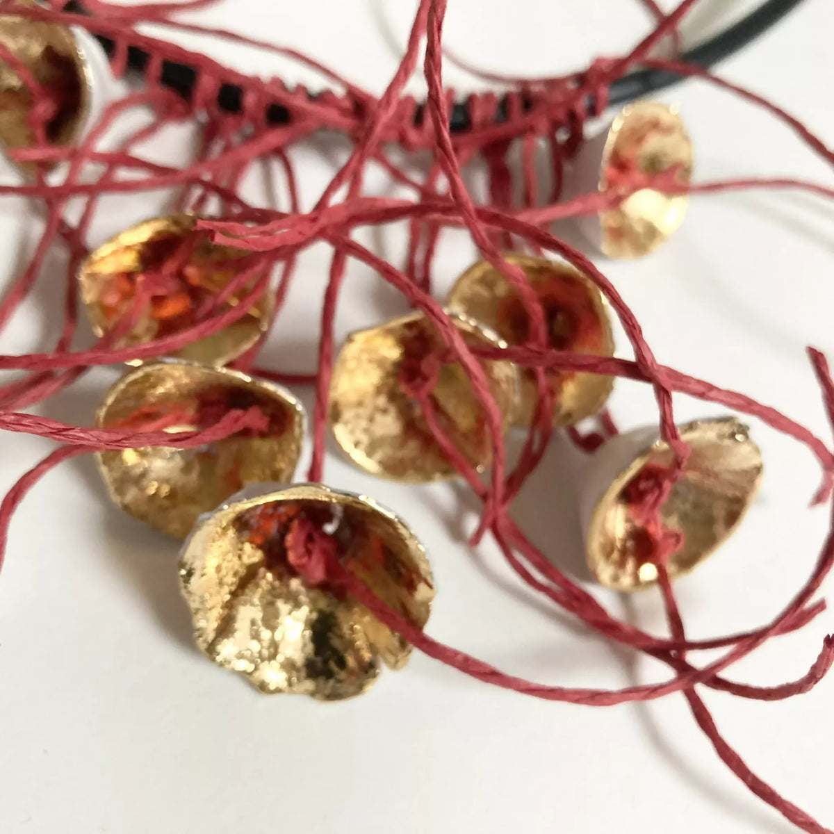 Collier aux fleurs dorées texturées et fils rouges, vue rapprochée