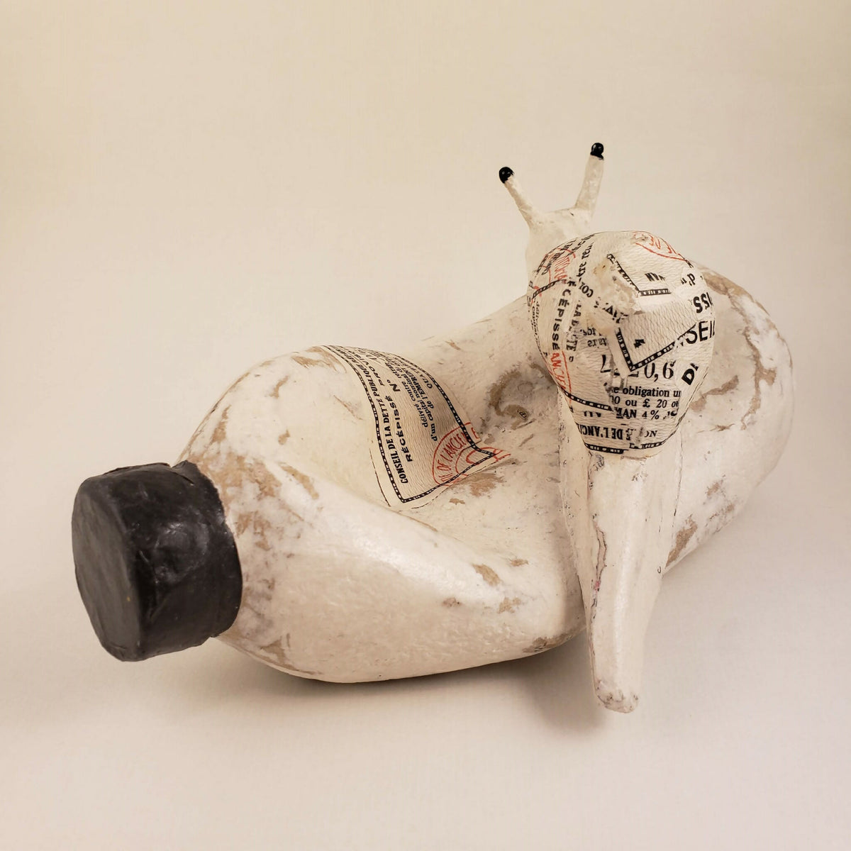 Sculpture d’escargot blanc, gros cylindre noir et coquilles imprimées façon papier.