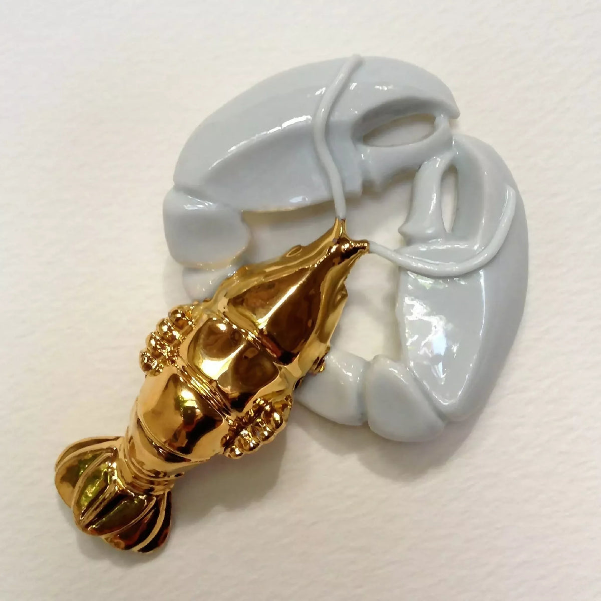 Porte-couvert homard blanc et doré, tête et pinces visibles, vue latérale.