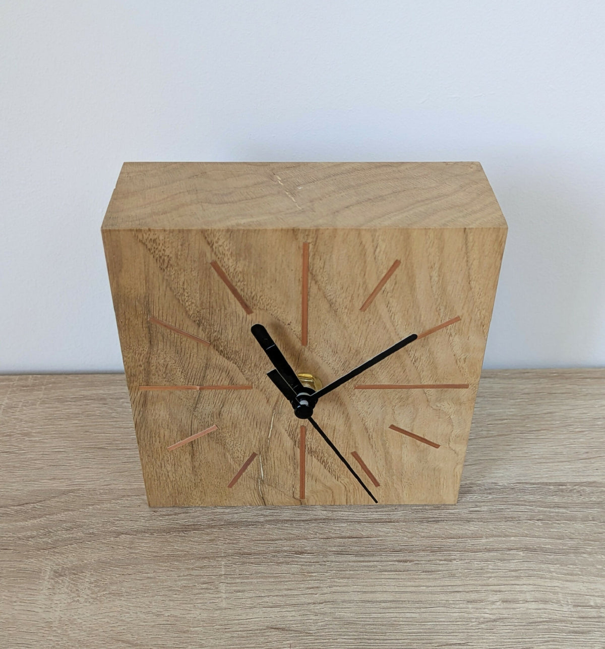 Horloge de bureau carrée en chêne clair, vue en angle, aiguilles noires et repères colorés.