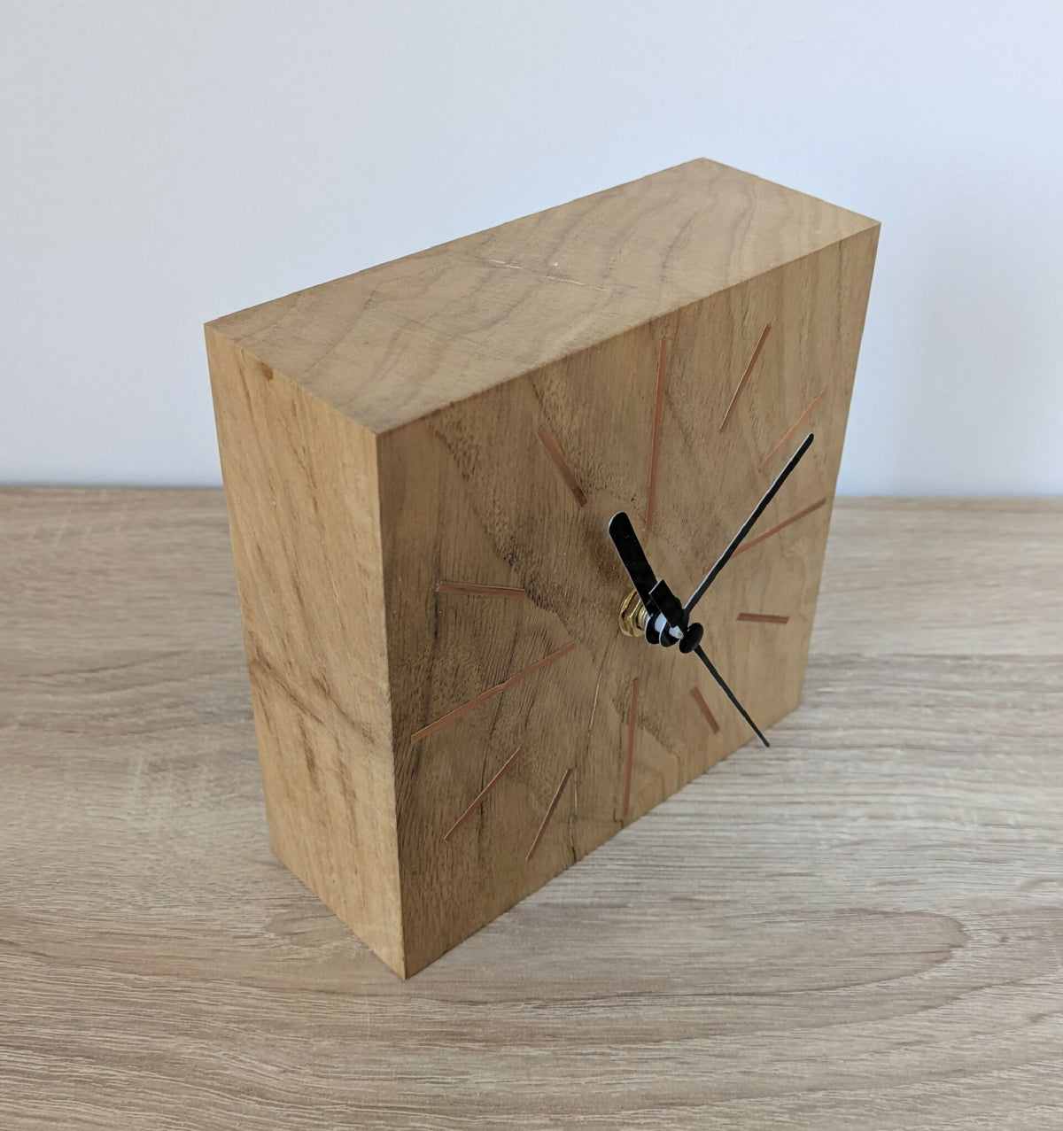 Horloge de bureau carrée en chêne clair, vue latérale avec cadran et aiguilles noires.