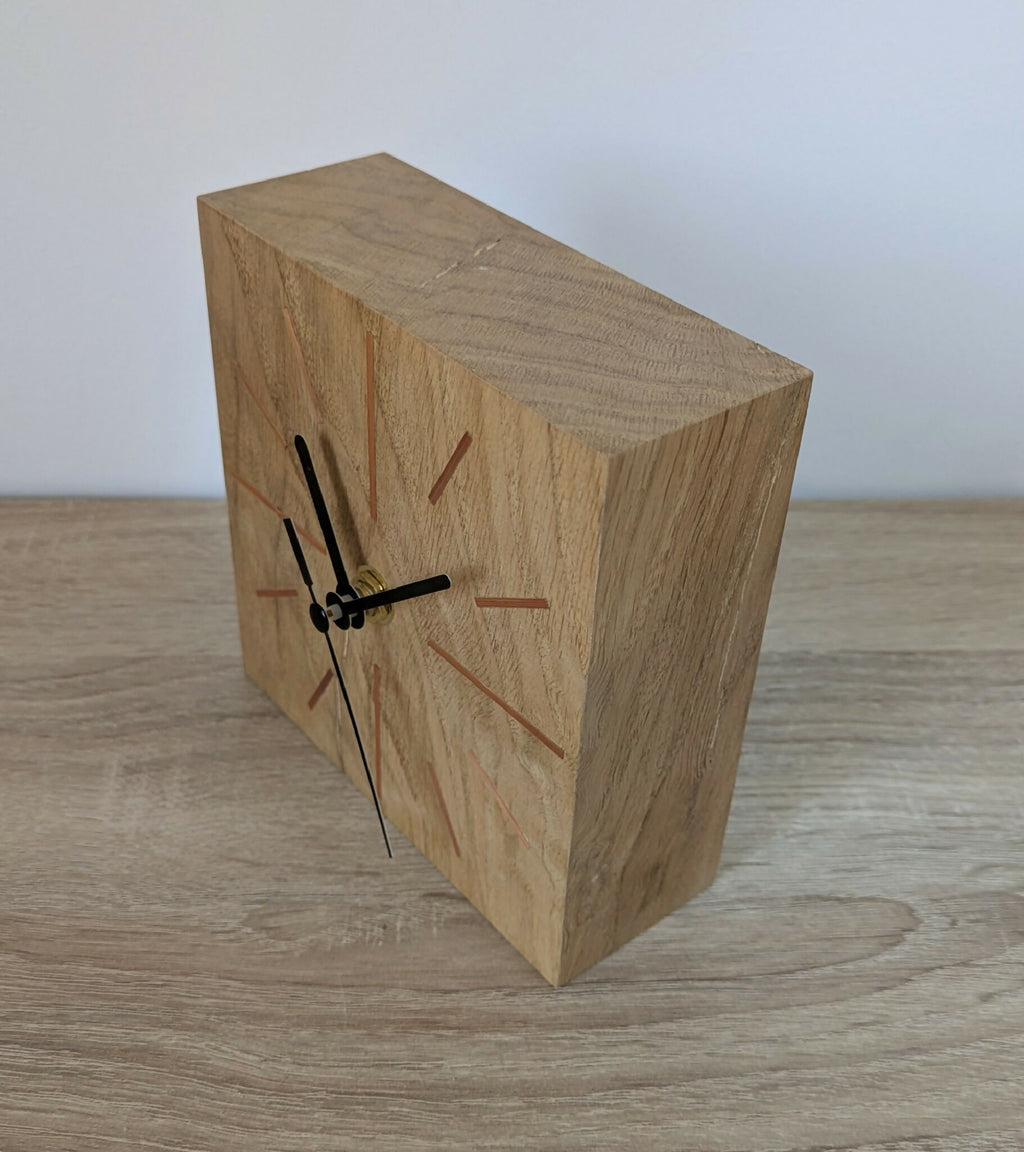 Horloge de bureau carrée en chêne clair, vue oblique, aiguilles noires et cadran à repères.