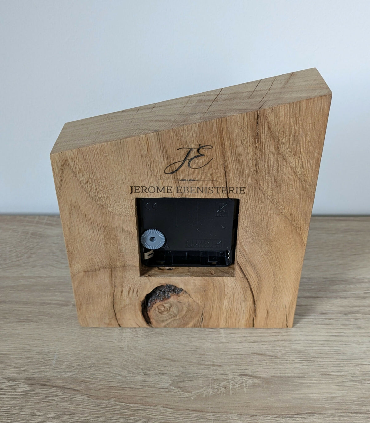 Horloge de bureau en bois clair avec mécanisme noir encastré et logo gravé.