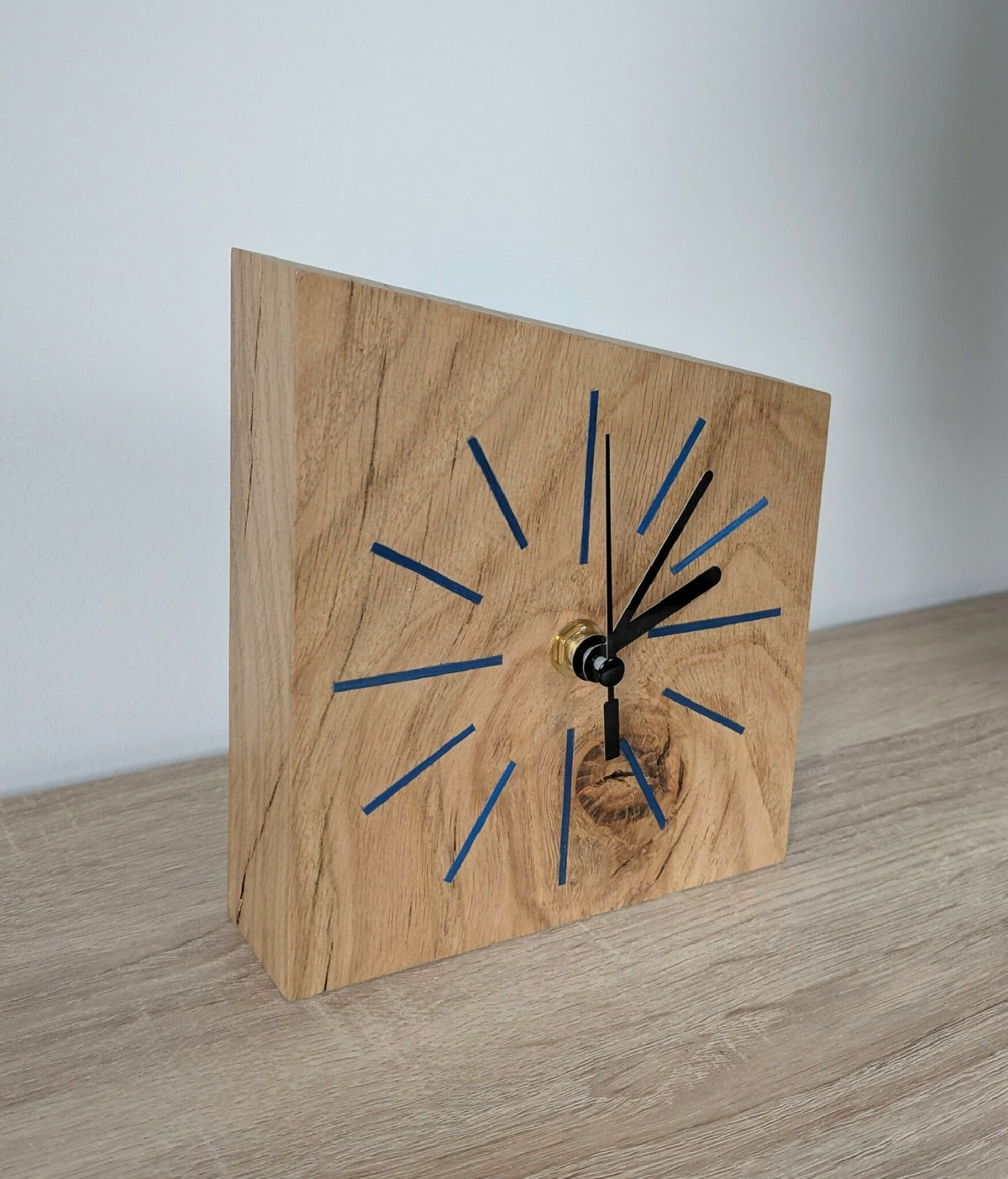 Horloge de bureau en bois clair sur pied, cadran bleu et aiguilles noires dorées.