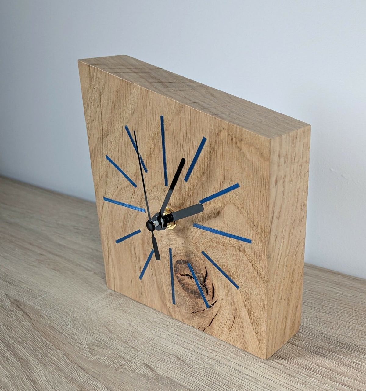 Horloge de bureau en bois clair, cadran à traits bleus, aiguilles noires et poignée.