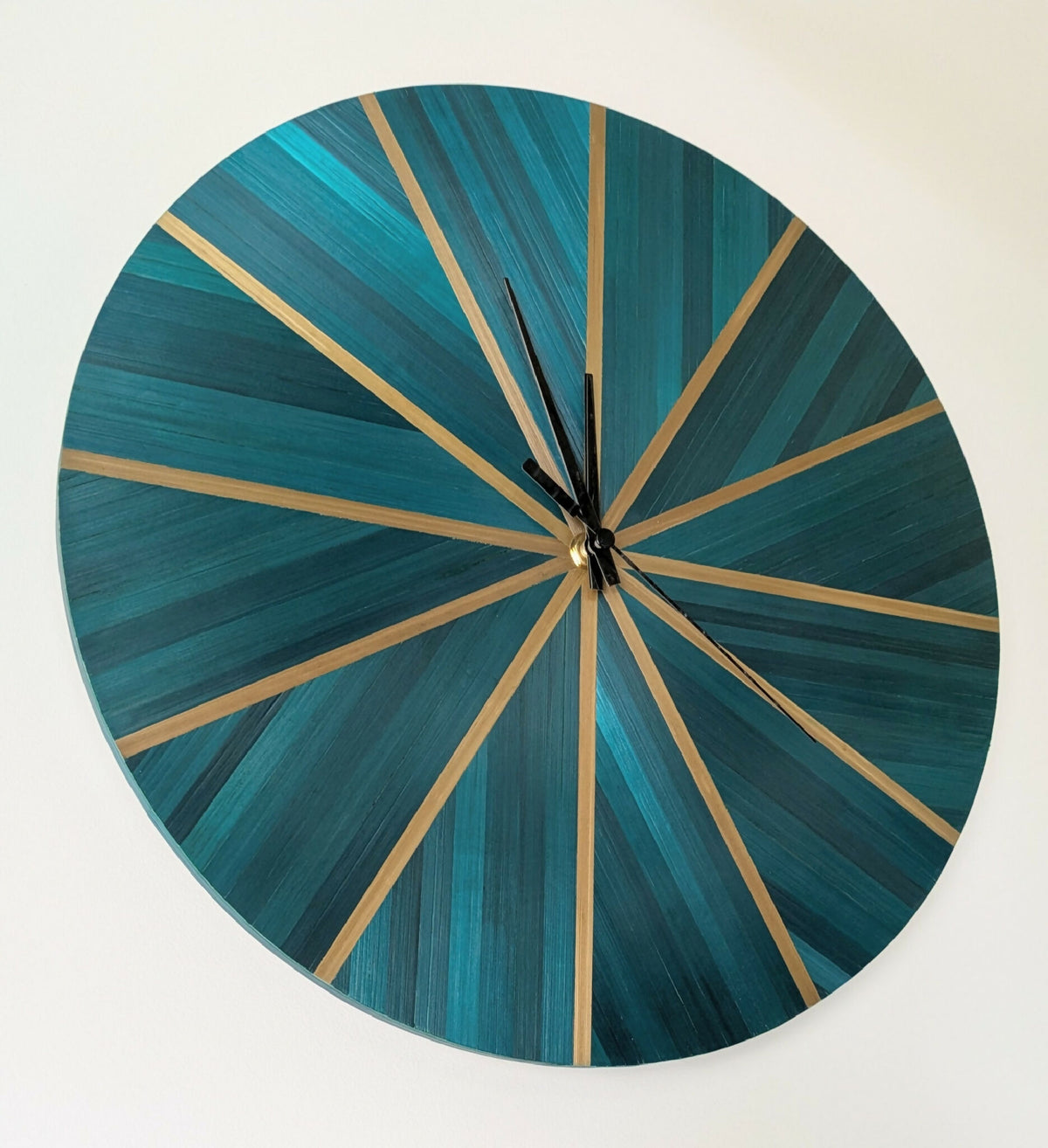 Horloge murale ronde en paille bleu-vert, rayons dorés, centre noir avec aiguilles