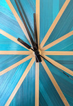 Horloge murale ronde : détail du centre noir avec aiguilles, rayons paille bleu-vert doré