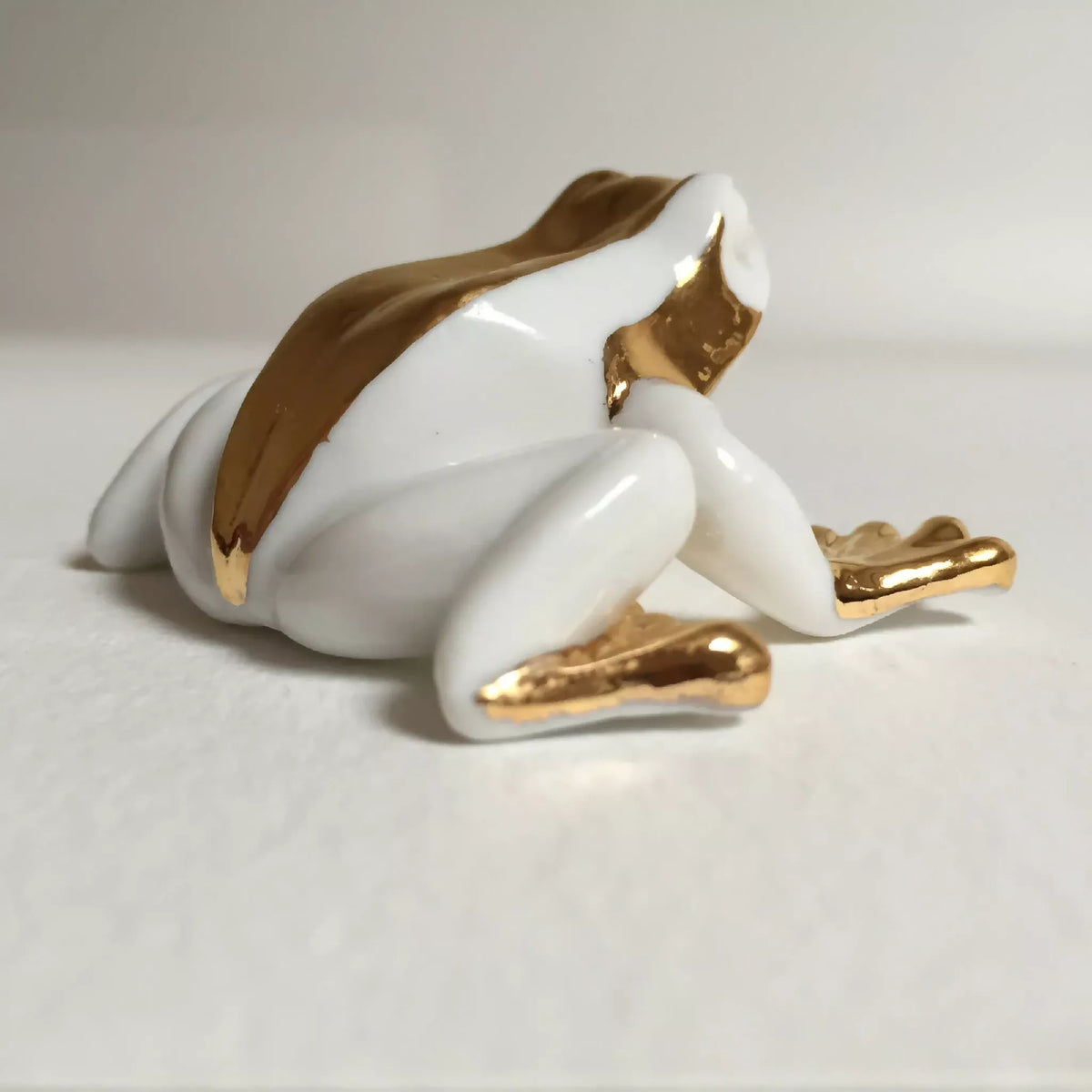 Figurine de grenouille en porcelaine blanche, vue de dos et pattes dorées