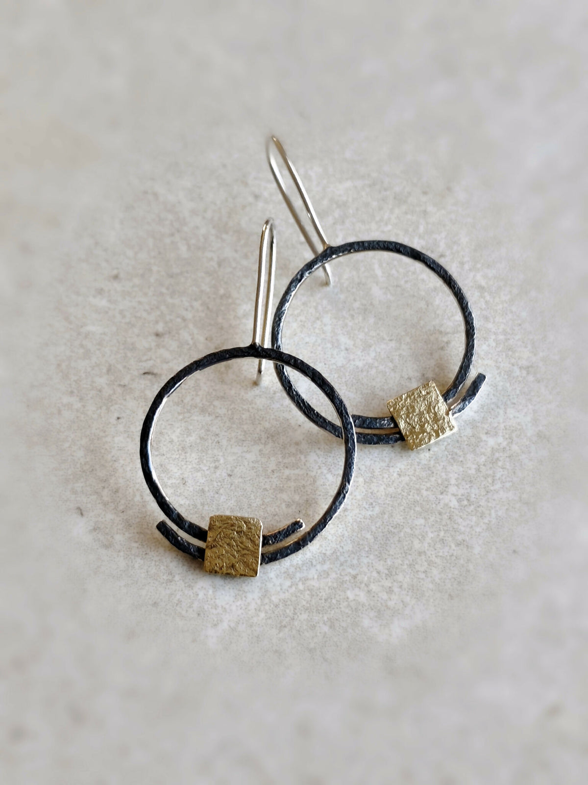 Paire de boucles d’oreilles pendantes : anneaux noirs, carrés dorés texturés, fermoirs à l’arrière.