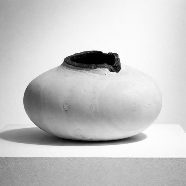 Vase céramique blanche à ouverture sombre sur le dessus, forme arrondie.