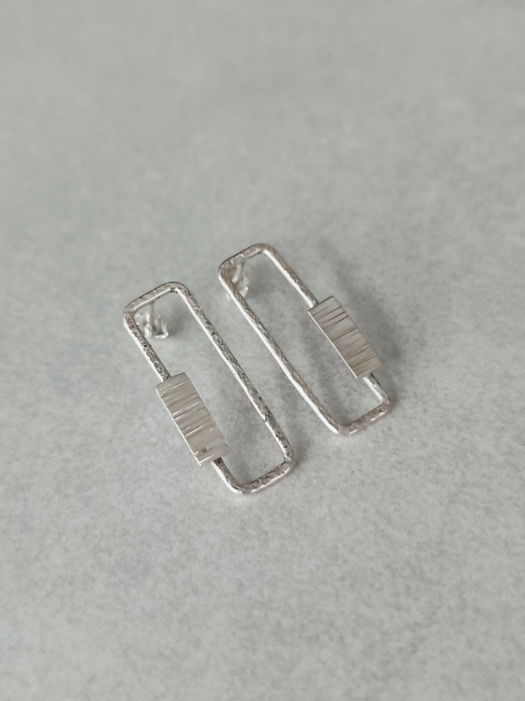 Boucles d’oreilles rectangulaires argentées, angle latéral sur la texture du centre.