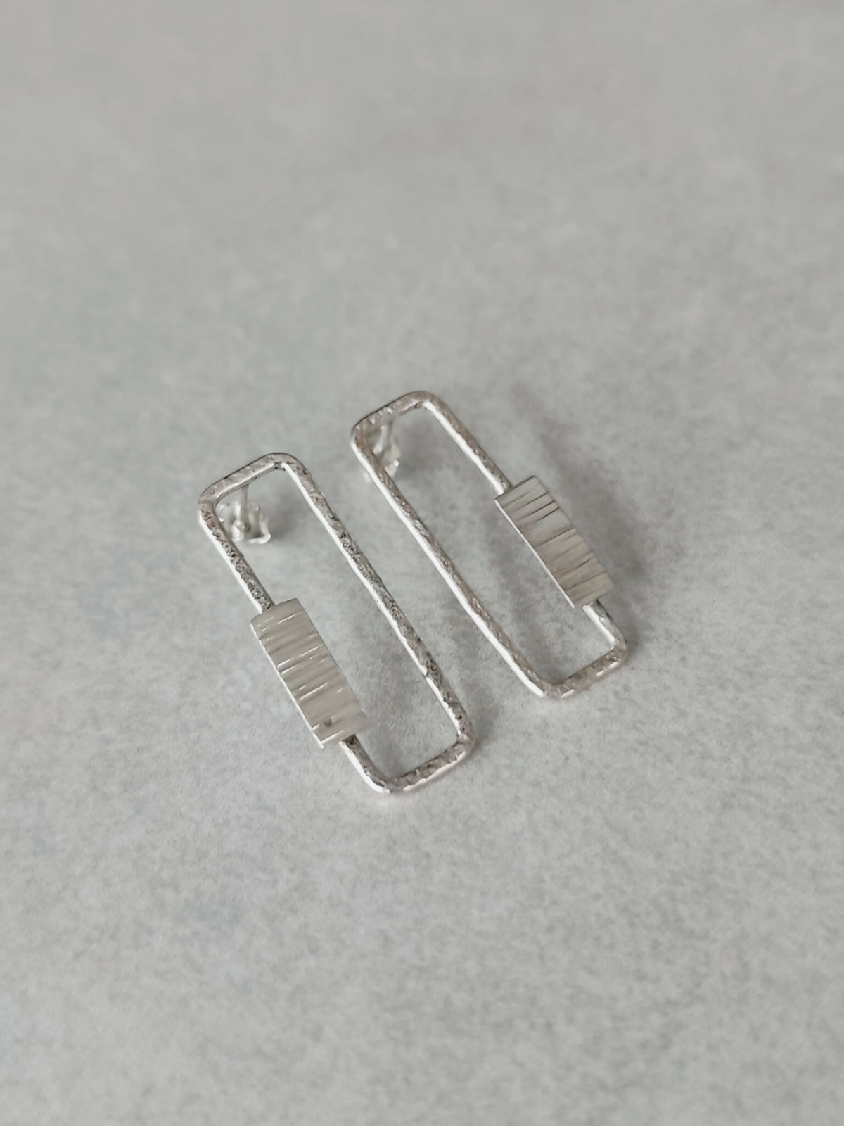 Boucles d’oreilles rectangulaires argentées, angle latéral sur la texture du centre.