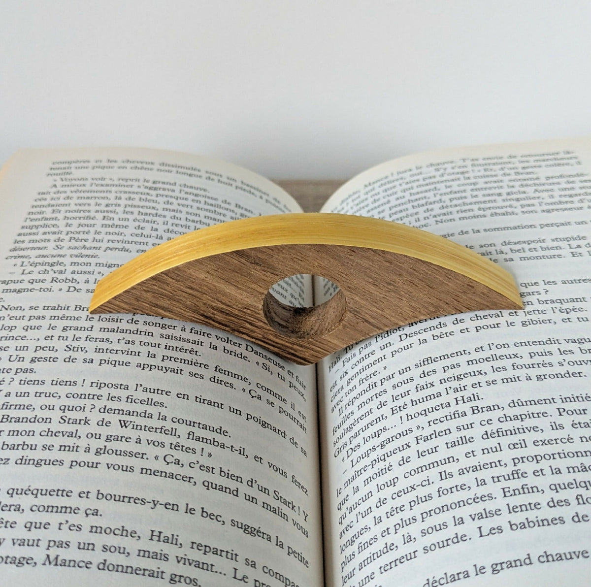 Anneau de lecture en bois marron avec marqueterie jaune, inséré dans un livre ouvert.